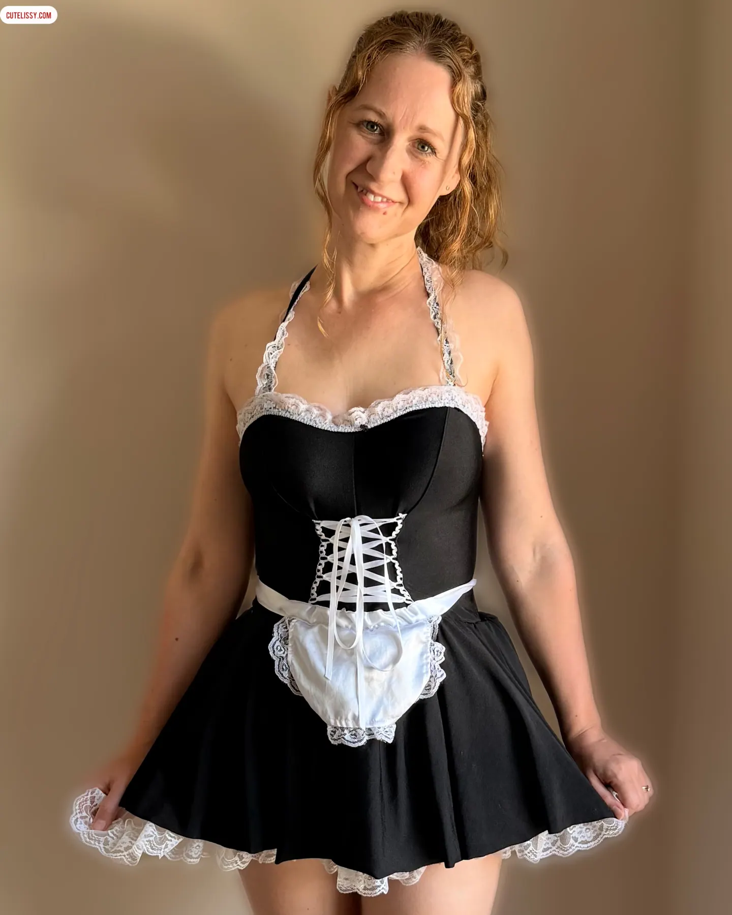 Lissy smiling and holding out the skirt of a black and white lace maid dress.